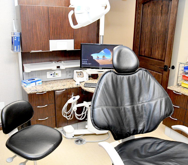 Dental treatment room with patient chair, assistant stool, computer monitor, and overhead dental equipment