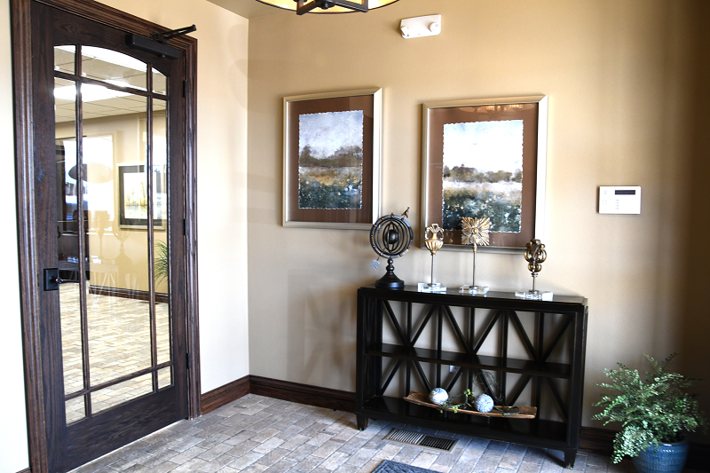 Professional office entryway with black French door, console table, framed mirrors, and neutral decor
