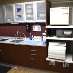 Sterilization and lab area with dark wood cabinetry, sink, autoclave equipment, and organized storage